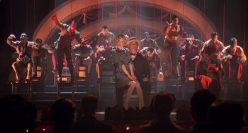 Movie still from “Chicago” (2002), directed by Rob Marshall – A man and a woman are sitting in front of a crowd; Wide shot, Low angle