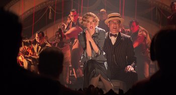 Movie still from “Chicago” (2002), directed by Rob Marshall – A man and a woman sitting on a bench in front of a group of people; Medium shot, Low angle
