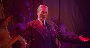 Movie still from “Chicago” (2002), directed by Rob Marshall – A man in a suit and tie standing in front of a group of people; Medium shot, Over the shoulder angle