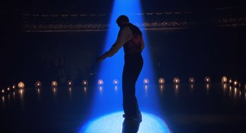 Movie still from “Chicago” (2002), directed by Rob Marshall – A man standing on one foot in a spotlight; Wide shot, Low angle