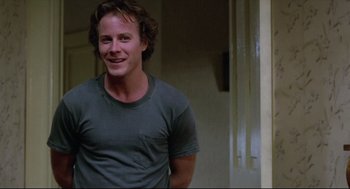 Movie still from “Chilly Scenes of Winter” (1979), directed by Joan Micklin Silver – A man smiling for the camera while standing next to a door; Medium shot, Over the shoulder angle