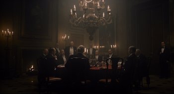 Movie still from “Darkest Hour” (2017), directed by Joe Wright – A group of people sitting around a table in front of a chandelier; Wide shot, Low angle