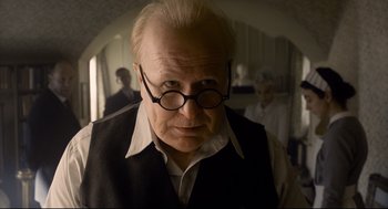 Movie still from “Darkest Hour” (2017), directed by Joe Wright – An older man wearing glasses and wearing a vest; Close Up shot, Over the shoulder angle