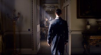 Movie still from “Darkest Hour” (2017), directed by Joe Wright – A man walking down a hall way in a suit; Wide shot, Low angle