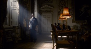 Movie still from “Darkest Hour” (2017), directed by Joe Wright – A man in a uniform standing in a living room; Wide shot, Low angle