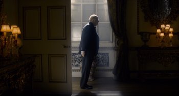 Movie still from “Darkest Hour” (2017), directed by Joe Wright – An older man standing in a doorway looking out a window; Medium shot, Low angle