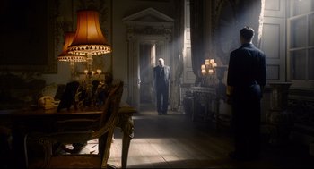Movie still from “Darkest Hour” (2017), directed by Joe Wright – A man in a suit and tie in a room with a table; Wide shot, Low angle
