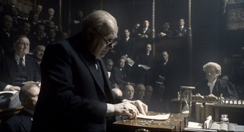 Movie still from “Darkest Hour” (2017), directed by Joe Wright – An old man in a black suit is writing on a piece of paper; Medium shot, Low angle