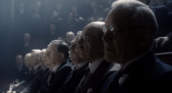 Movie still from “Darkest Hour” (2017), directed by Joe Wright – A group of men in suits sitting in front of a crowd; Wide shot, Low angle