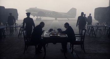 Movie still from “Darkest Hour” (2017), directed by Joe Wright – Two men sitting at a table in front of an airplane; Wide shot, Low angle