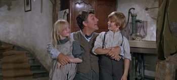 Movie still from “Chitty Chitty Bang Bang” (1968), directed by Ken Hughes – A man and two children are standing in a room; Medium shot, Low angle