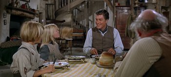 Movie still from “Chitty Chitty Bang Bang” (1968), directed by Ken Hughes – A man sitting at a table with a plate of food; Medium shot, Over the shoulder angle