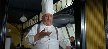 Movie still from “Chitty Chitty Bang Bang” (1968), directed by Ken Hughes – A man in a chef's hat holding a cross; Medium shot, Low angle