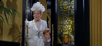 Movie still from “Chitty Chitty Bang Bang” (1968), directed by Ken Hughes – A woman and a child dressed as a woman and a boy in front of a window; Medium shot, Low angle