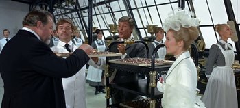 Movie still from “Chitty Chitty Bang Bang” (1968), directed by Ken Hughes – A group of people standing around a table; Medium shot, Over the shoulder angle