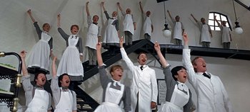 Movie still from “Chitty Chitty Bang Bang” (1968), directed by Ken Hughes – A group of people standing in front of a staircase; Wide shot, Low angle