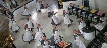 Movie still from “Chitty Chitty Bang Bang” (1968), directed by Ken Hughes – A group of women in aprons dancing in a room; Wide shot, Overhead angle