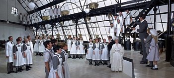 Movie still from “Chitty Chitty Bang Bang” (1968), directed by Ken Hughes – A group of people standing in front of a building; Wide shot, High angle