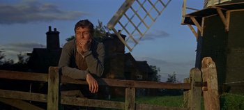 Movie still from “Chitty Chitty Bang Bang” (1968), directed by Ken Hughes – A man leaning on a fence near a windmill; Medium shot, Low angle