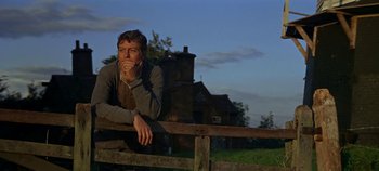 Movie still from “Chitty Chitty Bang Bang” (1968), directed by Ken Hughes – A man leaning on a wooden fence in front of a house; Medium shot, Low angle