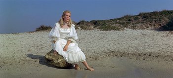 Movie still from “Chitty Chitty Bang Bang” (1968), directed by Ken Hughes – A woman in a white dress sitting on a rock on the beach; Wide shot, Low angle