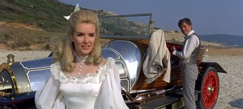 Movie still from “Chitty Chitty Bang Bang” (1968), directed by Ken Hughes – A woman in a white dress standing next to an old car; Medium shot, Low angle