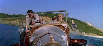 Movie still from “Chitty Chitty Bang Bang” (1968), directed by Ken Hughes – A group of people riding in the back of an old fashioned car; Wide shot, Low angle