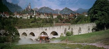 Movie still from “Chitty Chitty Bang Bang” (1968), directed by Ken Hughes – A man driving an antique car on a dirt road near a bridge; Extreme Wide shot, High angle