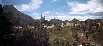 Movie still from “Chitty Chitty Bang Bang” (1968), directed by Ken Hughes – A castle in the middle of a town with mountains in the background; Extreme Wide shot, High angle