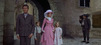 Movie still from “Chitty Chitty Bang Bang” (1968), directed by Ken Hughes – A group of people standing next to each other on a street; Medium shot, Low angle