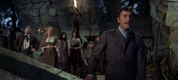 Movie still from “Chitty Chitty Bang Bang” (1968), directed by Ken Hughes – A group of people standing in front of a stone wall; Medium shot, Low angle
