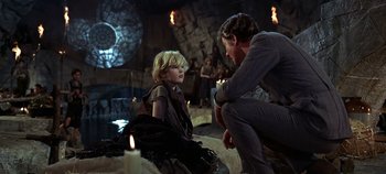 Movie still from “Chitty Chitty Bang Bang” (1968), directed by Ken Hughes – A man kneeling down next to a woman in front of candles; Medium shot, Over the shoulder angle