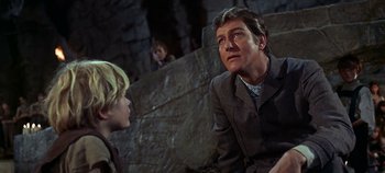 Movie still from “Chitty Chitty Bang Bang” (1968), directed by Ken Hughes – A man and a boy are sitting next to each other in front of a stone wall; Medium shot, Low angle