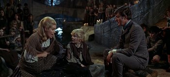 Movie still from “Chitty Chitty Bang Bang” (1968), directed by Ken Hughes – A group of people sitting on the ground in front of a body of water; Medium shot, Over the shoulder angle