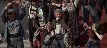 Movie still from “Chitty Chitty Bang Bang” (1968), directed by Ken Hughes – A group of people standing next to each other on a street; Medium shot, Low angle