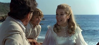 Movie still from “Chitty Chitty Bang Bang” (1968), directed by Ken Hughes – A group of people standing on top of a sandy beach; Medium shot, Over the shoulder angle