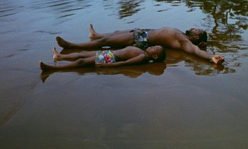 Movie still from “Chocolat” (1988), directed by Claire Denis – A man and a child are floating in the water; Wide shot, Overhead angle