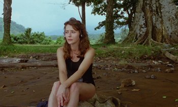 Movie still from “Chocolat” (1988), directed by Claire Denis – A woman sitting on top of a rock in a field; Medium shot, Low angle