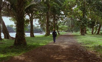 Movie still from “Chocolat” (1988), directed by Claire Denis – A woman walking down a dirt path through a forest; Extreme Wide shot, High angle