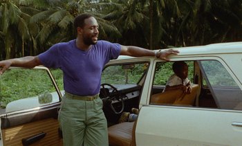Movie still from “Chocolat” (1988), directed by Claire Denis – A man standing in front of a parked car; Medium shot, Low angle