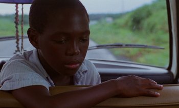 Movie still from “Chocolat” (1988), directed by Claire Denis – A young man sitting in a car looking out the window; Close Up shot, Over the shoulder angle