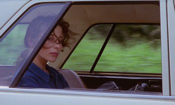Movie still from “Chocolat” (1988), directed by Claire Denis – A woman sitting in the driver's seat of a car; Close Up shot, Over the shoulder angle