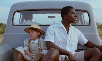 Movie still from “Chocolat” (1988), directed by Claire Denis – A man and a girl sitting on the back of a van; Close Up shot, Low angle