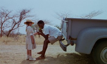 Movie still from “Chocolat” (1988), directed by Claire Denis – A man and a little girl standing next to a truck; Medium shot, Over the shoulder angle