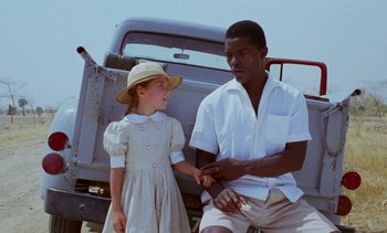 Movie still from “Chocolat” (1988), directed by Claire Denis – A man and a little girl standing next to a truck; Medium shot, High angle