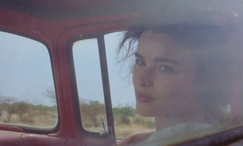 Movie still from “Chocolat” (1988), directed by Claire Denis – A woman sitting in the driver's seat of a car; Close Up shot, Over the shoulder angle