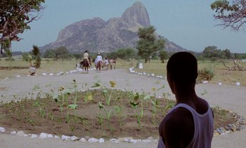 Movie still from “Chocolat” (1988), directed by Claire Denis – A man standing in front of a group of people on horses; Extreme Wide shot, Over the shoulder angle