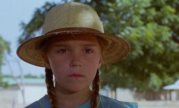 Movie still from “Chocolat” (1988), directed by Claire Denis – A young girl wearing a straw hat and braids; Close Up shot, Over the shoulder angle