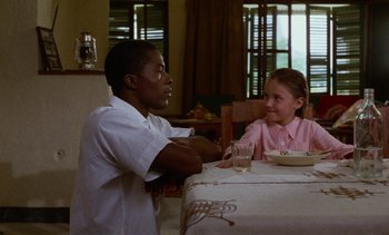 Movie still from “Chocolat” (1988), directed by Claire Denis – A man sitting at a table with a little girl; Medium shot, Over the shoulder angle