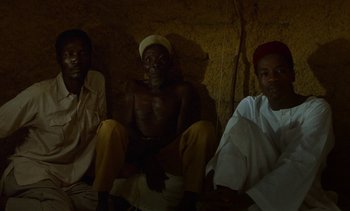 Movie still from “Chocolat” (1988), directed by Claire Denis – A group of men sitting next to each other in a room; Medium shot, High angle